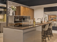 Moderne keuken met kookeiland, houten kastenwand en geïntegreerde apparaten, afgewerkt met zwarte kraan en barkrukken.